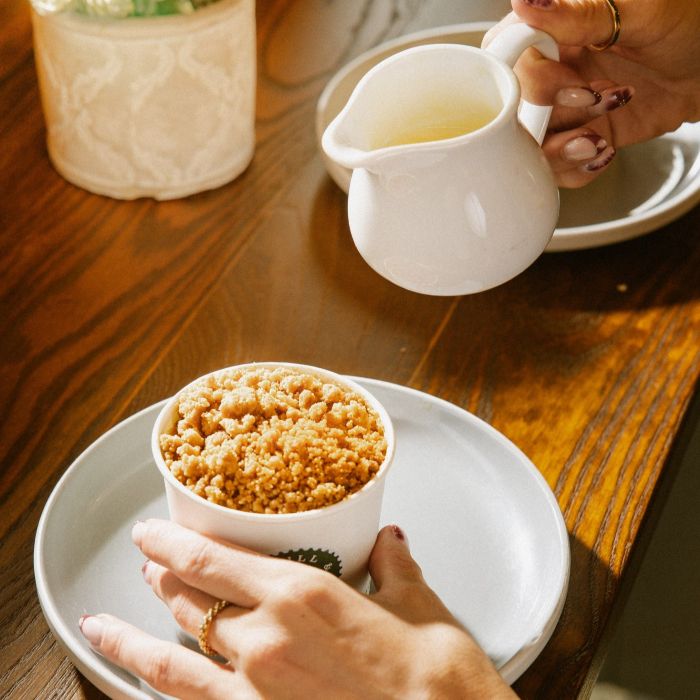 A lady topping a crumble pot with hot custard.